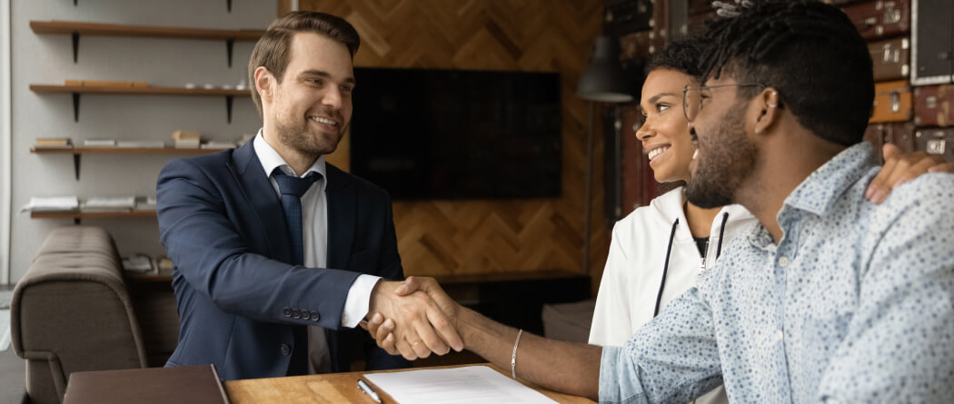 A man in a suit shaking hands with a young couple 